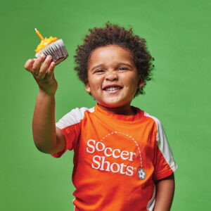 a child wearing soccer shots uniform holding a cupcake